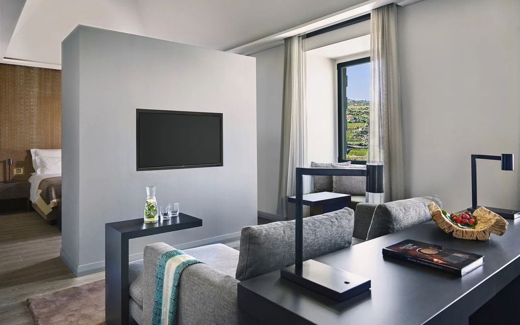 Elegant suite with vineyard views, featuring modern gray decor, king bed, plush seating area and floor-to-ceiling windows in Portugal