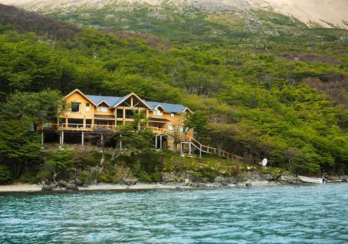 Rustic luxury lodge with wooden exterior nestled among snow-capped Andes mountains, reflecting in a pristine alpine lake at sunset