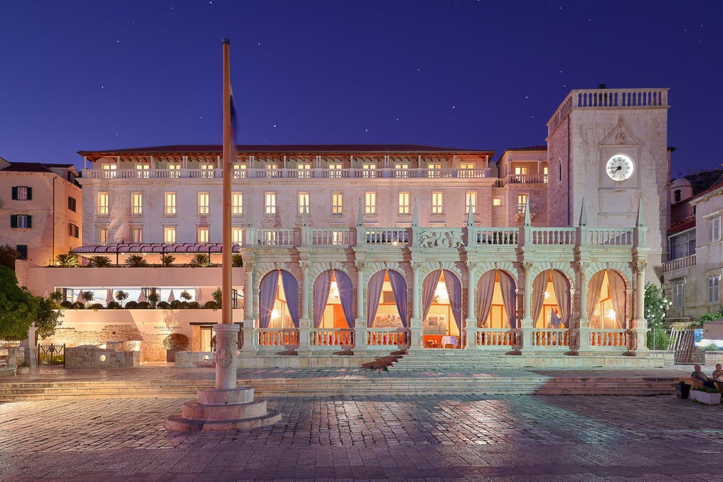 Five-star Hotel Palace Elisabeth rising above Hvar's harbor at sunset, featuring ornate beige facade and elegant Venetian architecture