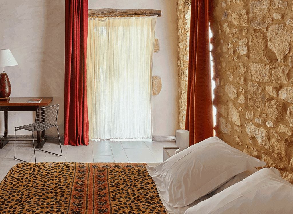 Elegant stone-walled suite with plush white bedding, antique furnishings, arched window overlooking French countryside at scenic hotel La Maison d'Ulysse