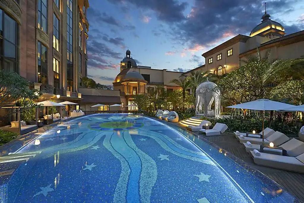 Modern luxury high-rise hotel in Taipei with art deco facade, glass windows, decorative lighting and manicured garden entrance at dusk