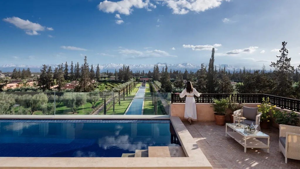 Luxurious Moroccan resort with traditional architecture, intricate tilework, palm trees, and a serene reflecting pool against a backdrop of Atlas Mountains.