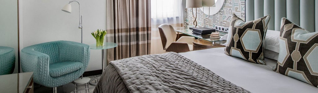 Elegant deluxe hotel room with luxurious queen bed, plush neutral decor, soft lighting, and sophisticated modern design in a premier UK boutique hotel