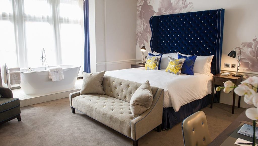 Elegant superior hotel room with crisp white linens, modern artwork, plush armchair, and soft neutral tones in a luxurious United Kingdom boutique setting