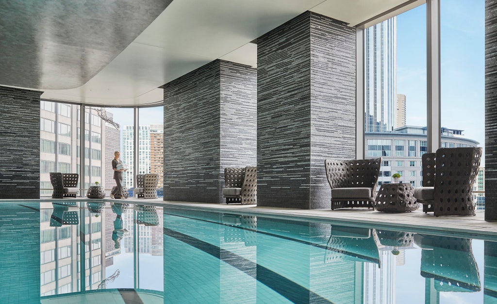 Luxury high-rise hotel tower with sleek glass exterior, soaring into Boston skyline against clear blue sky, reflecting clouds and sunlight