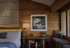 Luxurious Ventana Big Sur guestroom with elegant wood furniture, plush white bedding, and expansive windows overlooking scenic coastal landscape in California