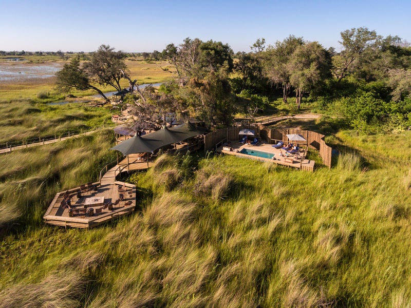 Elevated luxury safari camp with thatched-roof villas and wooden walkways overlooking Okavango Delta's pristine floodplains