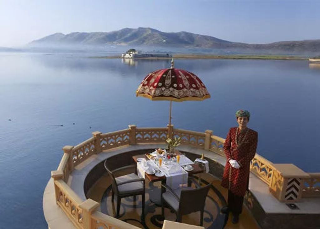 Luxurious lakeside palace hotel in Udaipur with ornate domes and archways, reflecting in Lake Pichola's calm waters at golden hour