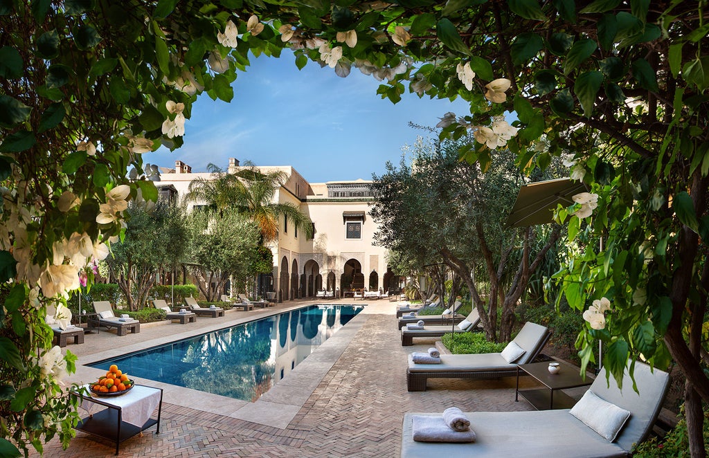 Traditional Moroccan luxury riad with ornate archways, tranquil courtyard pool surrounded by palm trees and orange trees in terracotta planters