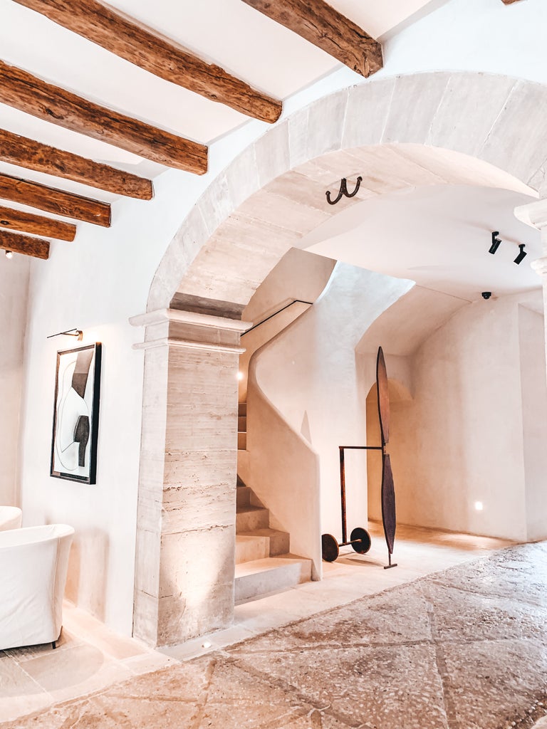 Sunlit courtyard of luxury Can Ferrereta hotel features rustic stone walls, lush greenery and elegant outdoor seating beneath archways