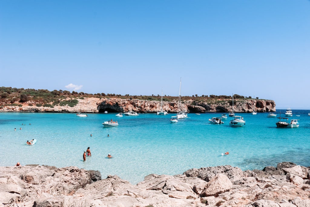 Luxurious white yacht anchored in crystal-clear turquoise waters of Port of Pollença, Mallorca, with scenic mountains and coastline in background