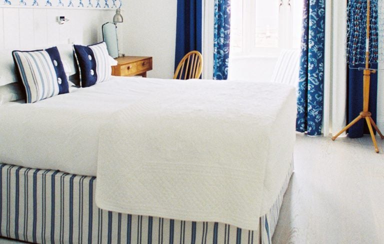 Elegant coastal hotel room with crisp white linens, sea-view window, minimalist decor, and soft blue accents overlooking scenic United Kingdom harbor landscape