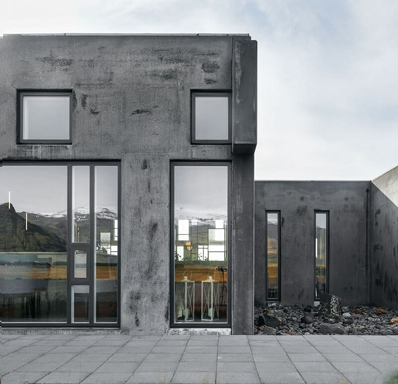 Modern, glass-walled hotel room overlooking snowy Icelandic mountains at dusk, featuring infinity pool and minimalist Nordic design