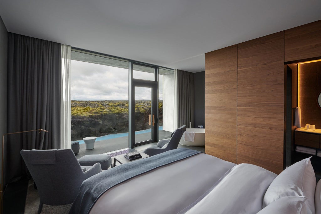 Luxurious lagoon-view suite with floor-to-ceiling windows, minimalist Nordic design, plush white bedding, and panoramic scenset landscape in Iceland.