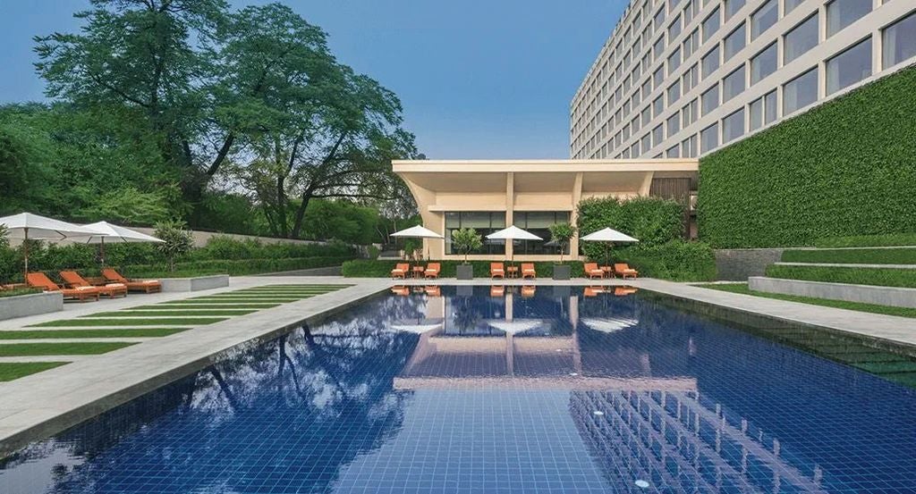 Elegant white marble entrance of The Oberoi Delhi hotel with ornate columns, crystal chandeliers and lush landscaped gardens at twilight