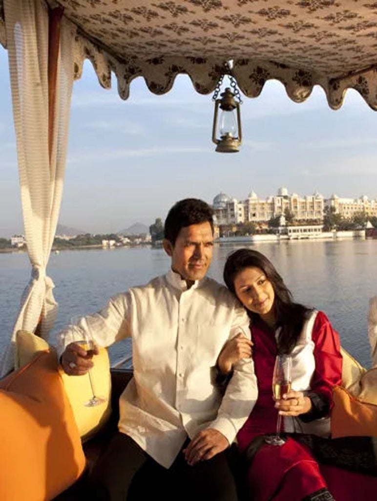 Grand lakeside palace hotel in Udaipur with ornate domes and archways, reflecting in Lake Pichola at golden hour with mountains beyond