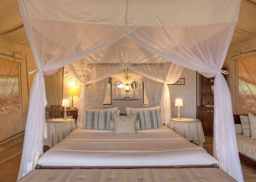 Elegant safari tent interior with vintage colonial decor, four-poster bed, antique furnishings and warm ambient lighting in Kenya