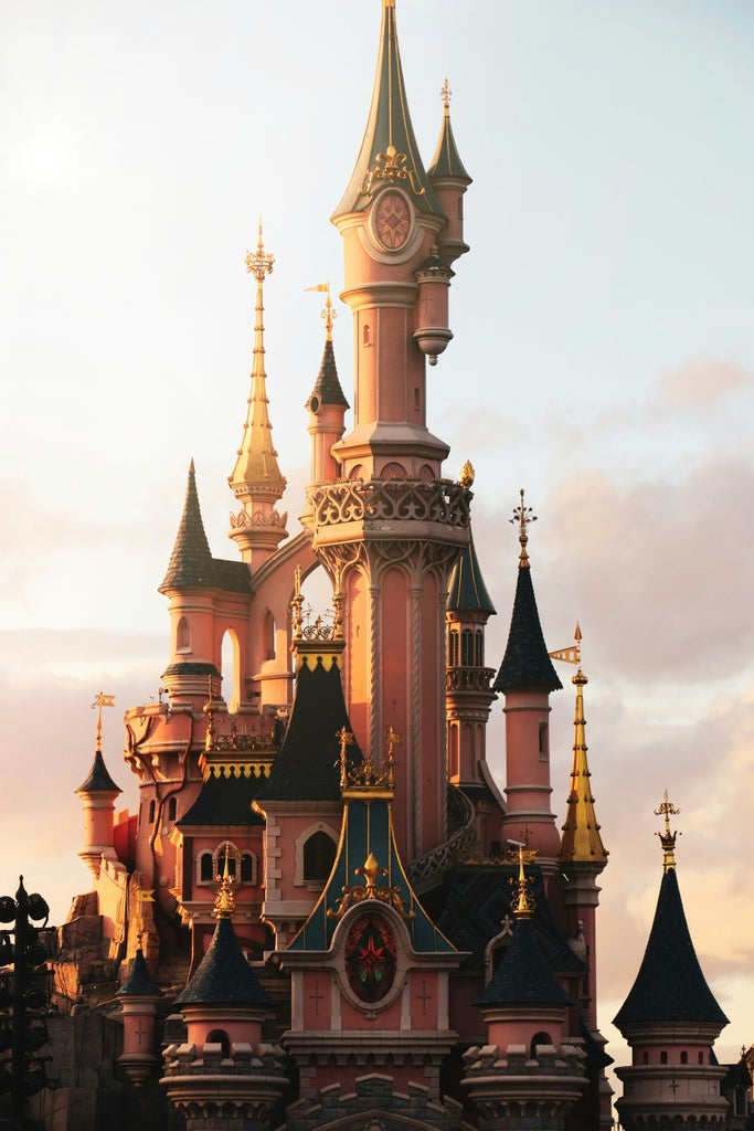 Magical Disneyland Paris castle at sunset, illuminated with golden lights, enchanting Disney characters posing in foreground with elegant park landscape