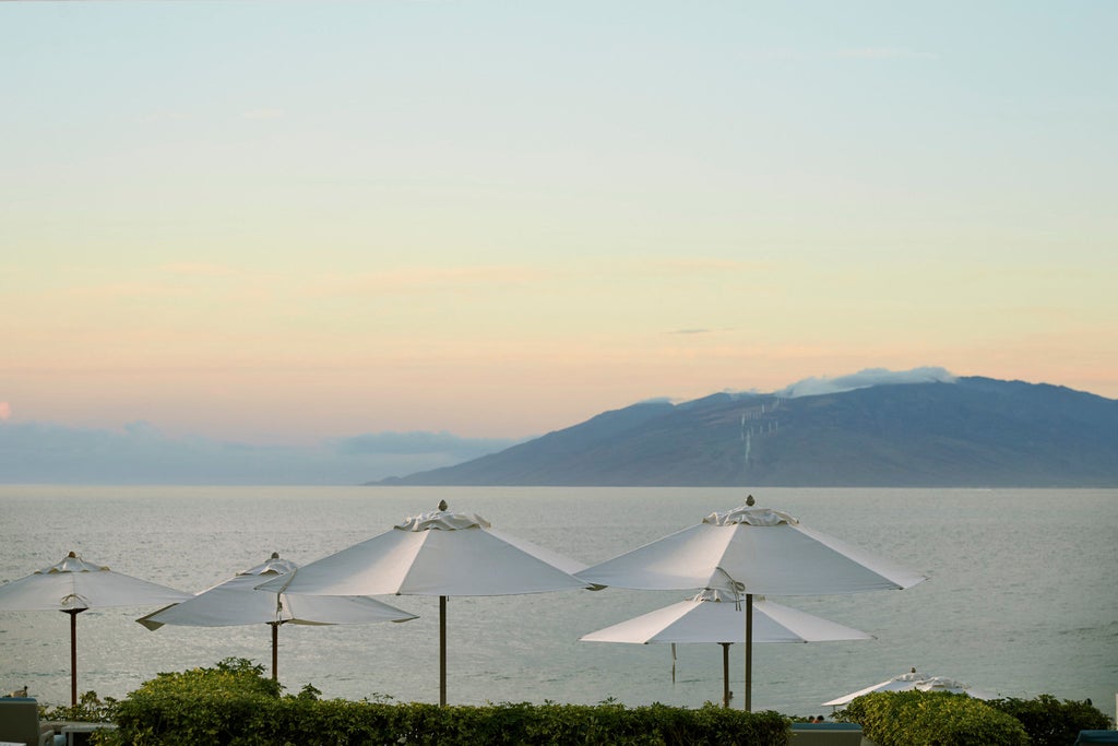 Luxurious beachfront resort with infinity pool overlooking the Pacific Ocean, palm trees and private cabanas at sunset in Maui, Hawaii