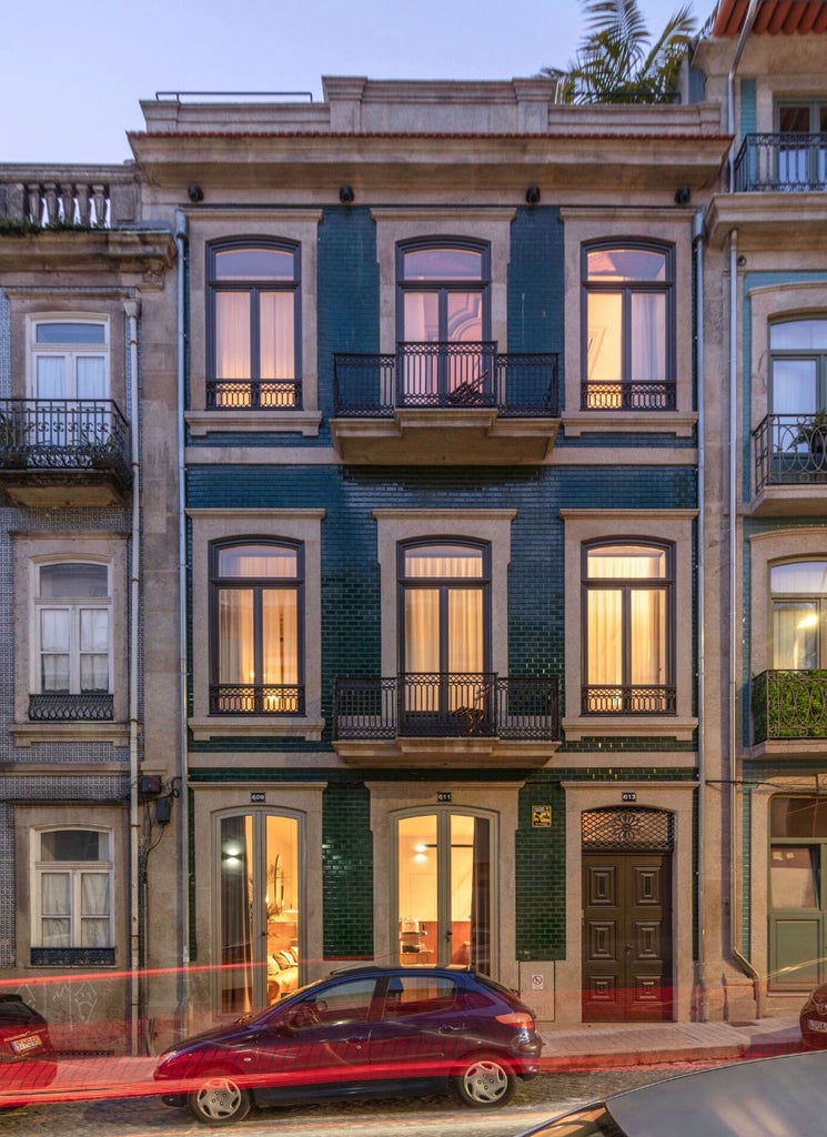 Elegant whitewashed boutique hotel with green shutters, wrought-iron balconies, and lush gardens framing the traditional Portuguese facade