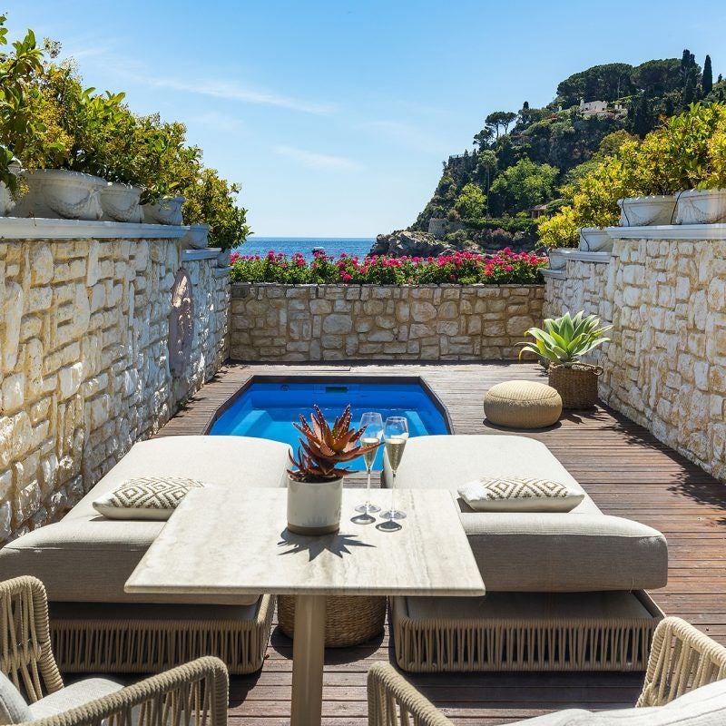 Elegant suite with private infinity pool overlooking Mediterranean Sea, featuring white loungers and panoramic coastal views of Taormina