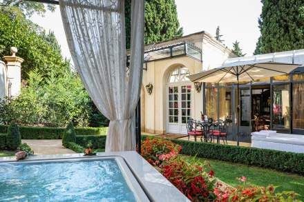 Elegant French Provençal hotel room with lavender-toned walls, antique wooden furniture, crystal chandelier, and plush white linens at Villa Gallici