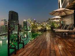 Modern illuminated Bangkok skyline at dusk, with luxurious high-rise buildings reflecting in Chao Phraya river under vibrant orange sky