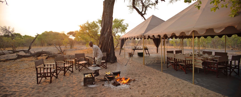 Luxury safari tent with elegant wooden deck overlooking Botswana's wilderness at sunset, featuring canvas walls and traditional furnishings