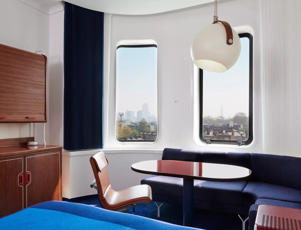 Sleek, modern hotel room with floor-to-ceiling windows overlooking London's urban skyline, featuring minimalist design and luxurious contemporary furnishings