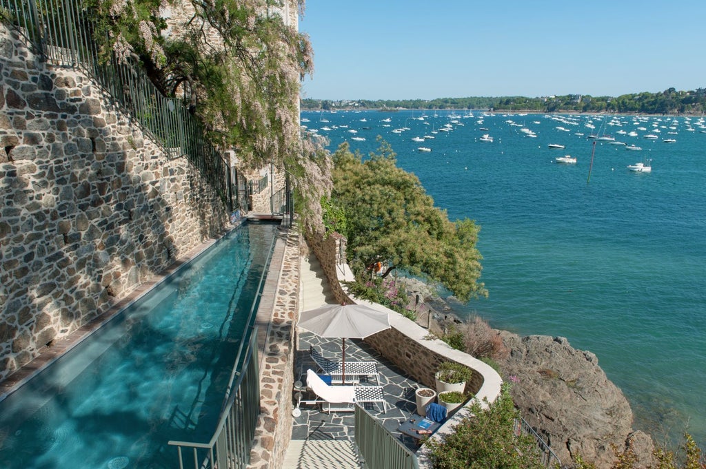 Luxurious seaside hotel with blue-grey facade, nestled on rocky coastline of Brittany, offering elegant architecture and panoramic ocean views