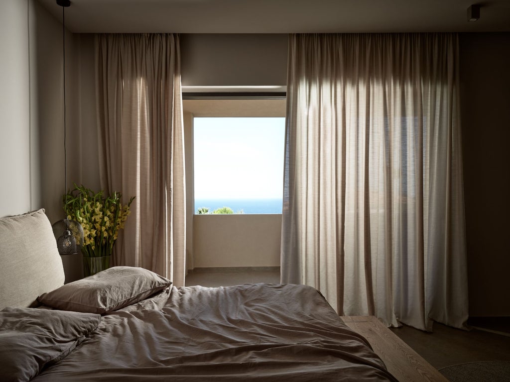 Luxurious Greek villa bedroom with white walls, elegant wooden furnishings, plush king bed, and panoramic Mediterranean sea view through expansive windows