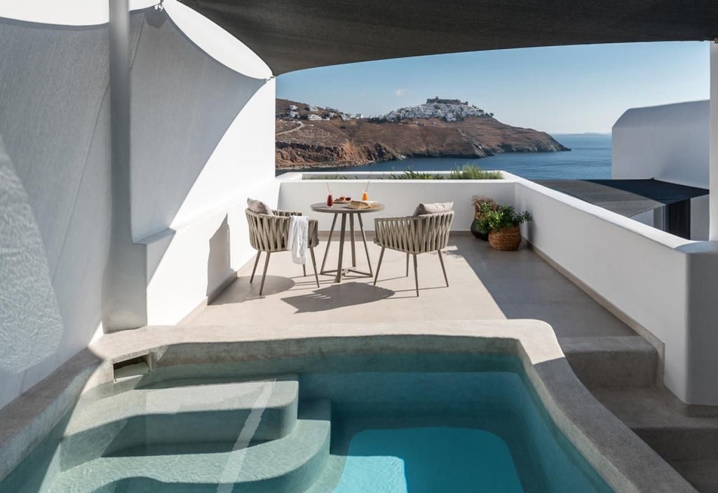 Elegant Greek honeymoon suite with white minimalist design, panoramic Aegean Sea view, plush bed, and private balcony overlooking scenic coastline