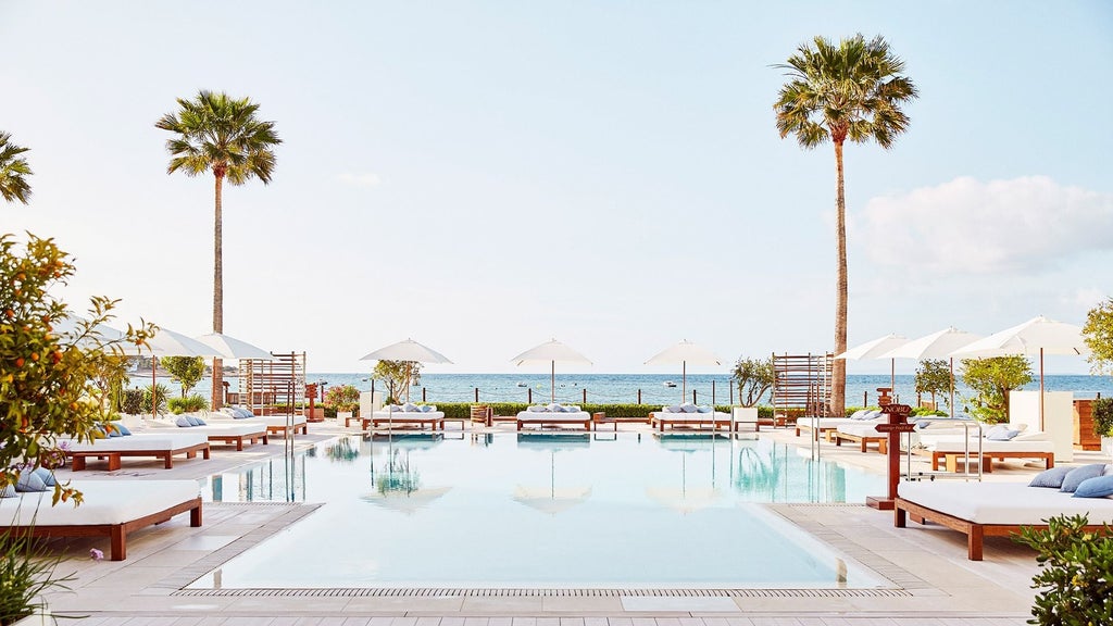 Elegant beachfront hotel with white Mediterranean architecture, infinity pool overlooking turquoise sea, and luxury loungers with cabanas