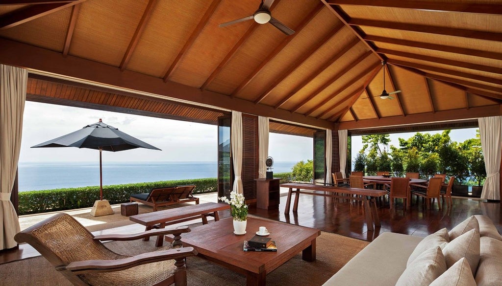 Luxurious infinity pool overlooking lush tropical gardens at sunset, with elegant villa and private lounge chairs framed by palm trees