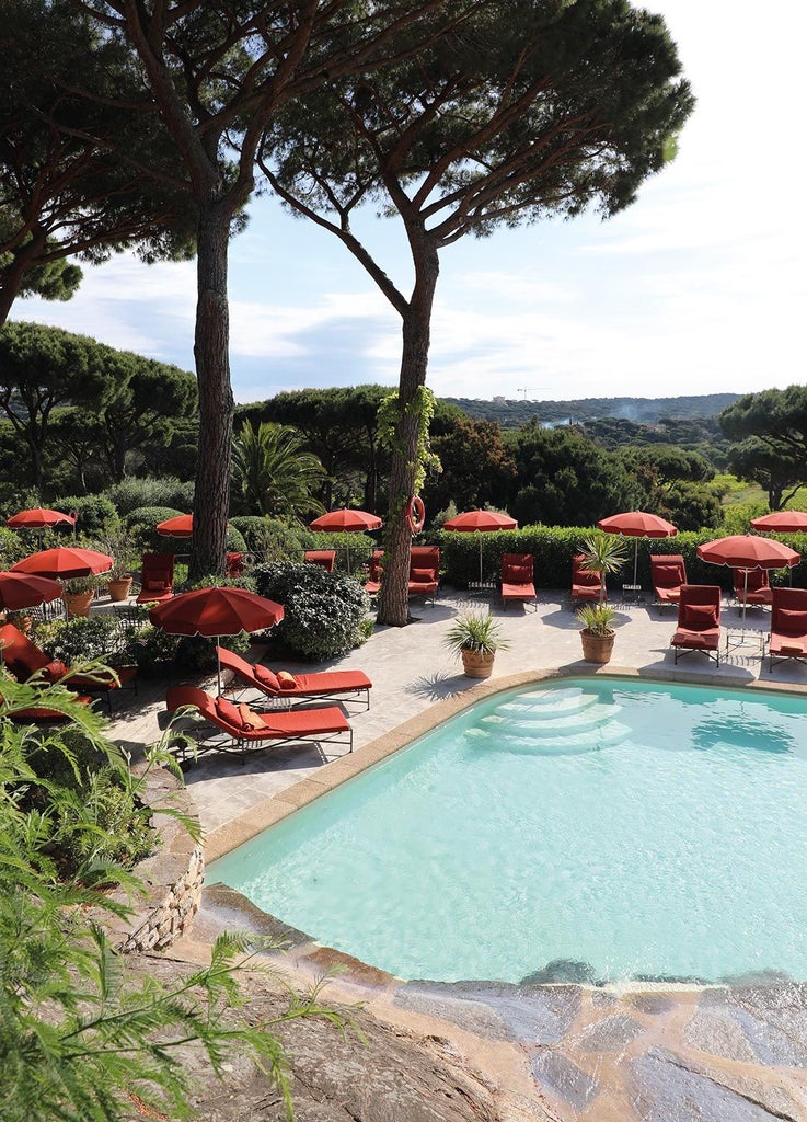 Luxurious white Mediterranean villa with blue shutters nestled among lush tropical gardens in Saint-Tropez, featuring elegant terrace and vibrant bougainvillea flowers