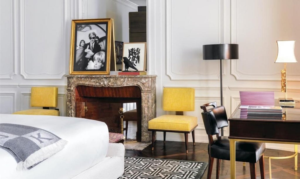 Elegant Parisian hotel suite with plush white bed, soft gray textiles, designer furniture, and large windows overlooking a chic urban landscape in soft morning light