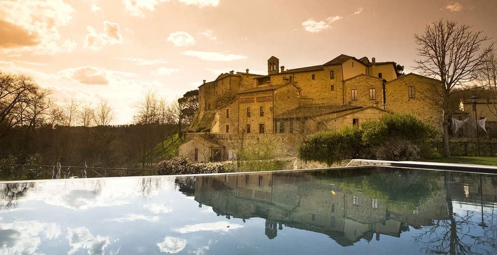 Luxurious stone monastery-turned-hotel in Tuscany with cypress trees, manicured gardens and traditional Italian architecture at sunset