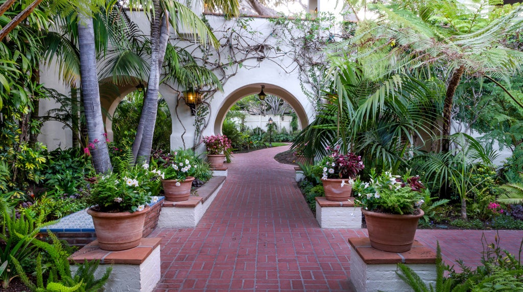 Spanish Colonial-style luxury beachfront resort with white stucco walls, red tile roofs, and lush palm gardens overlooking Pacific Ocean