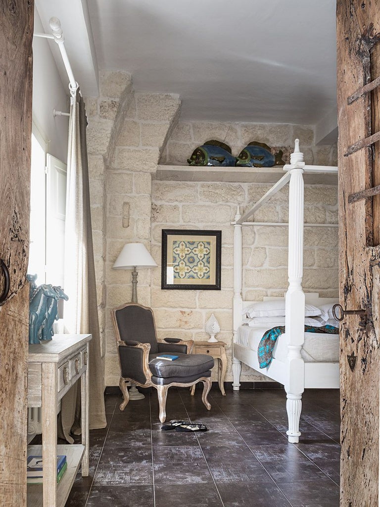 Elegant stone-walled Italian hotel room with arched windows, antique wooden furniture, and soft natural light in a historic Puglia mansion