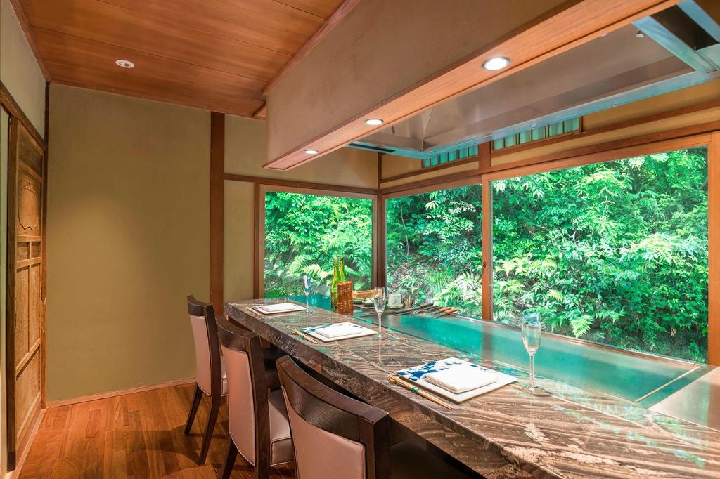 Traditional Japanese luxury ryokan with wooden architecture nestled among autumn trees along Arashiyama's riverbank in Kyoto