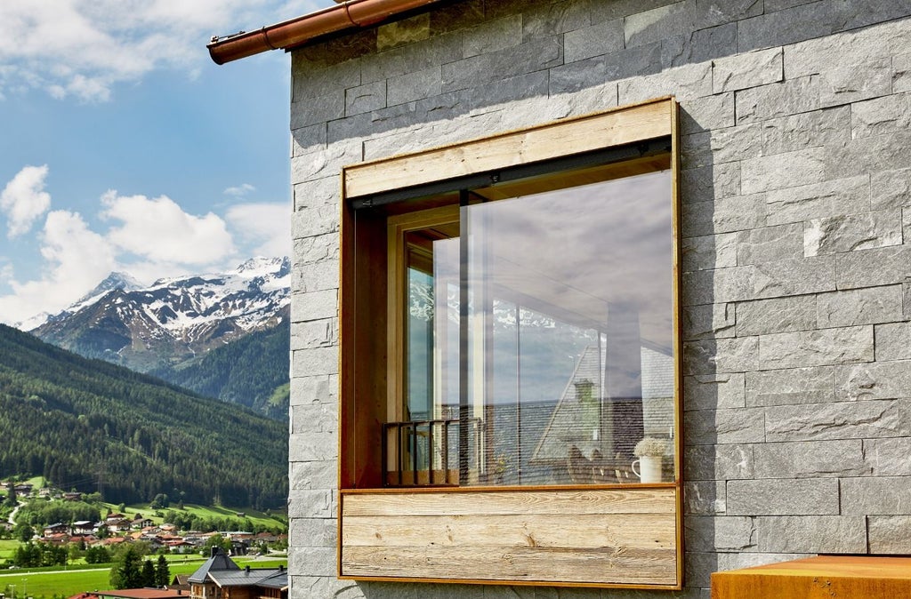 Luxurious mountain hotel nestled in Austrian Alps with traditional timber facade, stone base, and snow-capped peaks in background