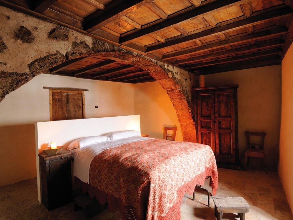 Rustic stone-walled superior room at Sextantio Albergo Diffuso, featuring traditional wooden bed, soft linens, and warm ambient lighting in medieval Italian setting