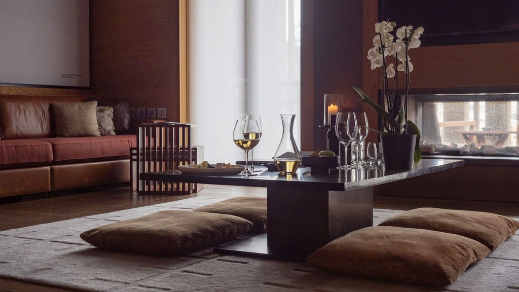 Elegant Swiss alpine hotel room with minimalist dark wood furnishings, plush white bedding, and panoramic mountain views through floor-to-ceiling windows.