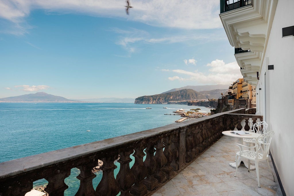 Opulent Italian suite with panoramic Mediterranean coastline view, elegant white furnishings, and soft natural light streaming through large windows