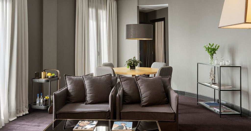 Spacious two-bedroom luxury suite with elegant modern decor, plush king beds, city view windows, and sophisticated neutral color palette in Madrid hotel