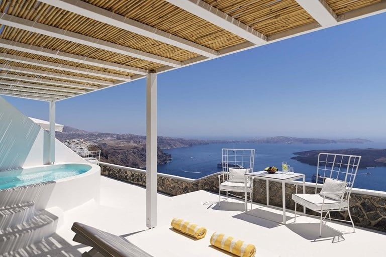 Whitewashed luxury hotel with blue-domed architecture perched on Santorini's cliff, overlooking the azure Aegean Sea with elegant infinity pools.