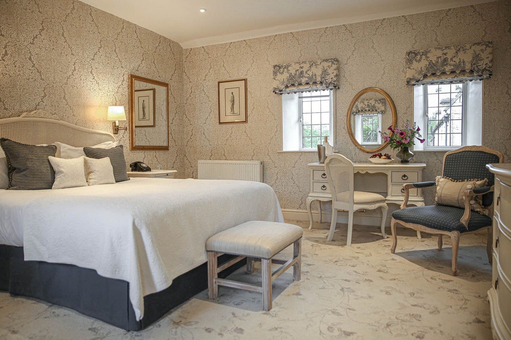 Elegant manor room at luxury hotel, featuring plush king bed, ornate fireplace, soft neutral tones, and classic British countryside decor with refined sophistication