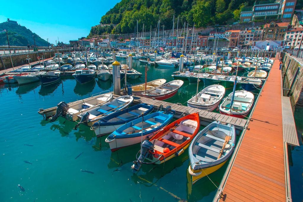 Sun-drenched seaside town in Basque Country with vibrant old buildings, luxury yachts in harbor, and dramatic cliffs along coastline