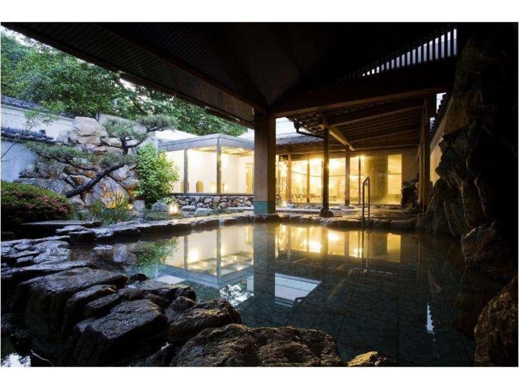 Traditional Japanese ryokan exterior with wooden facade, featuring illuminated lanterns and a serene entrance surrounded by manicured gardens