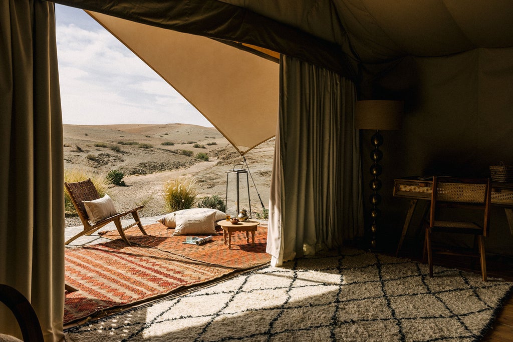 Desert luxury camp with elegant white canvas tents nestled among rolling sand dunes at sunset, featuring private terraces and mountain views